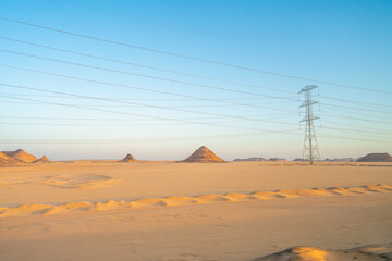 A stunning view of power lines crossing the desert landscape at sunrise in Aswan, Egypt, showcasing the beauty of the arid terrain and the infrastructure.