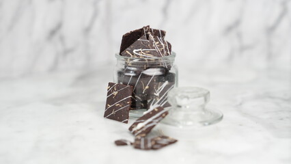 Crispy brownies arranged on a glass jar and white ceramic plate with a white marble background....