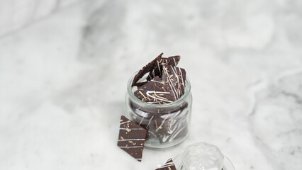 Crispy brownies arranged on a glass jar and white ceramic plate with a white marble background....