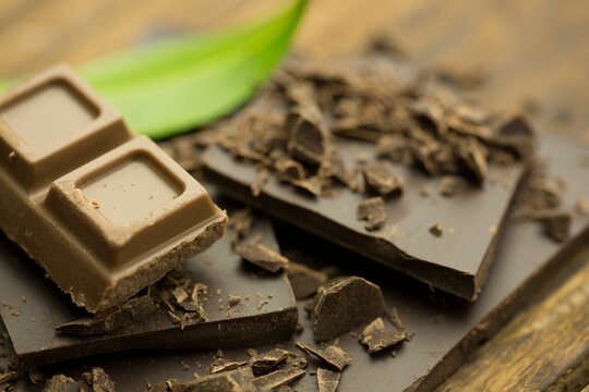 Naklejki 3D render showing milk and dark chocolate pieces resting on rustic wooden board with green leaf