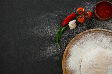 Pizza dough with flour and ingredients on table