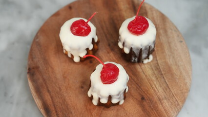 Three pieces of Chanelle cheesecake with white chocolate topping and red cherries placed on a round wooden plate