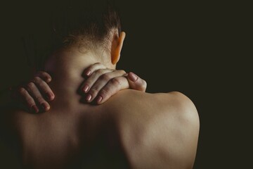 Bare-shouldered woman is reaching up to neck in flat design, directional lighting, dark backdrop
