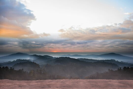 Fototapeta Misty hills and rocky plateau edge are featuring flat design with sun rays and mist layers