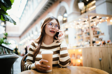 A stylish young woman with glasses and braces smiles at the camera, holding a coffee cup in a warmly lit cafe setting.