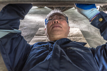 Senior Asian male auto mechanic fixing underneath car in auto repair shop