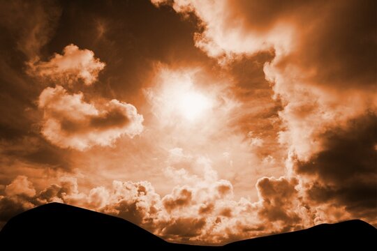 Fototapeta Bright sun is peeking through dense orange clouds in flat design dusk sky, with silhouetted hills