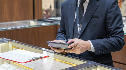 Close-up of a professional jeweler in a suit holding a calculator and pen at a luxury jewelry store...