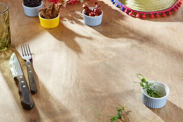 Wooden table with spices and utensils in bright overhead flatlay, Mexican menu background