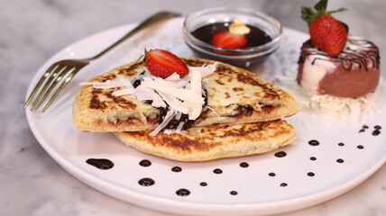 Chewy potato bread is arranged on a white plate and topped with cheese, strawberries and melted chocolate.