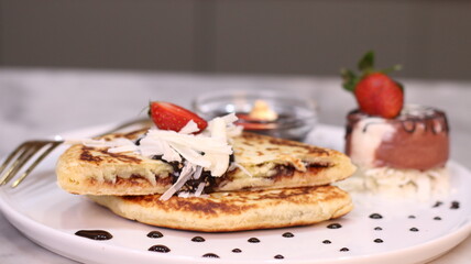Chewy potato bread is arranged on a white plate and topped with cheese, strawberries and melted chocolate.