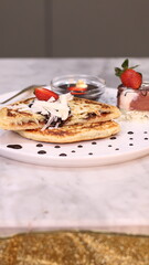 Chewy potato bread is arranged on a white plate and topped with cheese, strawberries and melted chocolate.