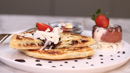 Chewy potato bread is arranged on a white plate and topped with cheese, strawberries and melted chocolate.