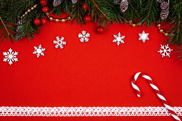 Christmas decorative set with green spruce, cones, holly berries, candy cane, white lace on red background, top view.
