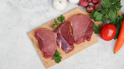 fresh raw meat on a cutting board with soup vegetables on the side. top view
