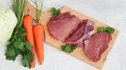 fresh raw meat on a cutting board with soup vegetables on the side