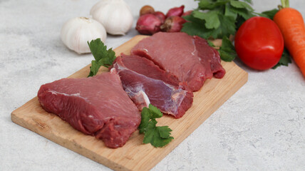 fresh raw meat on a cutting board with soup vegetables on the side
