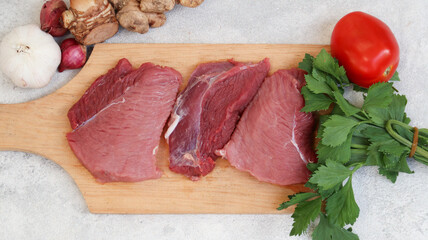 fresh raw meat on a cutting board with soup vegetables on the side. top view. flatlay