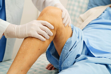 Doctor checking Asian elderly woman patient with scar knee replacement surgery in hospital.