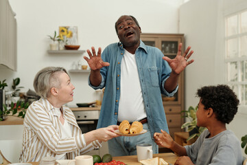 Family having breakfast together in modern kitchen, sharing food and laughter. Man appearing to...