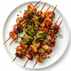 A white plate with skewered yakitori chicken, garnished with green onions, isolated on a white background