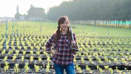 Confident young female farmer standing in lush plant nursery with pitchfork, symbolizing empowerment, agriculture, sustainability, and organic farming lifestyle