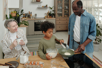 Multiethnic family spending time together in warm kitchen while father teaching child to cook,...