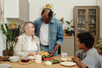 Married couple enjoying breakfast with their young child in cozy kitchen setting, showcasing multiethnic bonding and cultural diversity in harmonious atmosphere