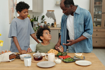 Senior man interacting with two children at breakfast table, sharing joyful moment in homey kitchen...