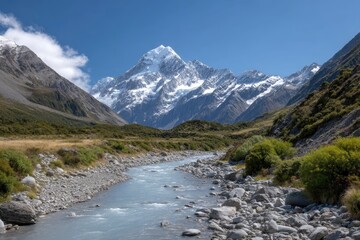 Fototapeta premium A river runs through a valley framed by snowcapped mountains under a blue sky