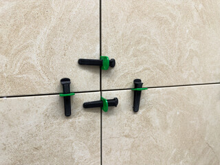 Ceramic wall tiles being installed with reusable leveling system. Black wedges and green spacers...