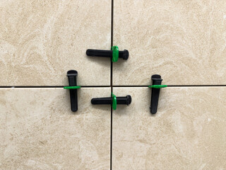 Close up of beige ceramic tiles aligned with tile leveling system. Precision tools create straight...