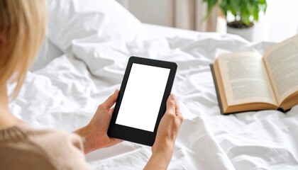 Woman relaxing in bed reading e book on digital tablet device White bedding and book nearby