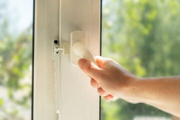 Hand operating a window handle to open a window during daylight in a residential setting