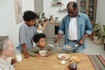 Family enjoying breakfast at a cozy kitchen table with pancakes, milk, and bread, creating warm and bonding moments while engaging in conversation and meal preparation