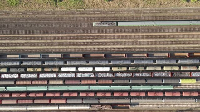 An aerial video of a large railway station shows multiple freight trains on parallel tracks while a passenger train passes through.