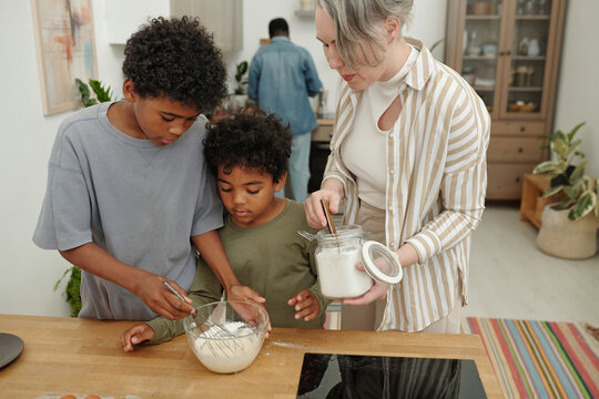 Mother and two children mixing ingredients in kitchen for baking project. Family bonding over cooking activity with focused expressions