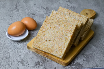Close up view of whole wheat sliced bread on wooden cutting board with two chicken eggs. grey or gray cement as background.