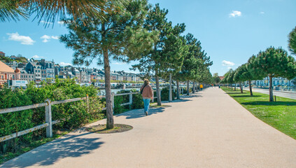 Walking along a scenic promenade by the riverside with tall trees and charming buildings in the background on a sunny day