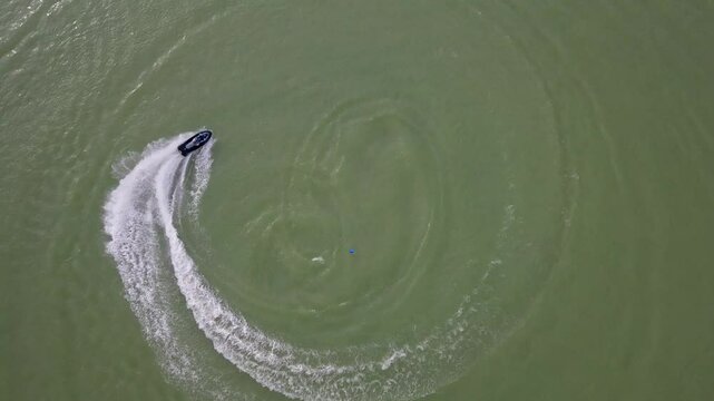 Jetskier is turning on his jet boat, waverunner across the water in a top view.
