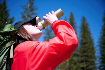 Woman in hiking gear taking a sip of water during mountain hike. Sporty female standing in front of...