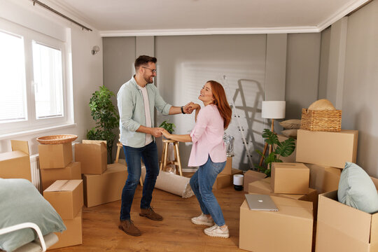 Couple dances happily in the midst of a newly vacated home, surrounded by unpacked boxes and a welcoming atmosphere. Their joyful expressions capture the excitement of moving in together.