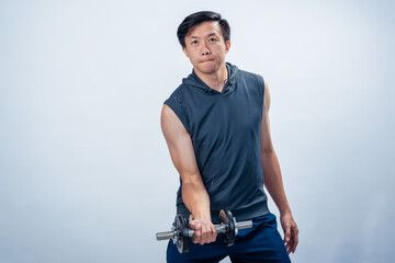 Asian man in sleeveless hoodie lifting dumbbell with one arm in controlled motion, standing with...