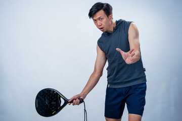 Asian man in sleeveless hoodie and shorts holding padel racket prepares for swing with focused face...
