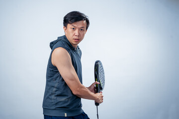 Asian man in sleeveless hoodie and shorts holding black padel racket in ready position, focused and...