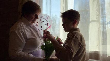 A cute boy gives his grandmother a bouquet of red tulips for her birthday, mother's day, anniversary. Warm family relationship between grandson and senior granny. - Powered by Adobe