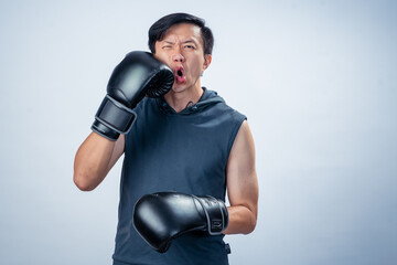 Asian man in sleeveless hoodie gets punched in the face with boxing glove during training, showing...