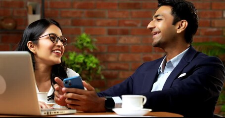 Indian business people using smartphone in office break, closeup of Asian corporate man and woman in professional attire casually scrolling social media or photos on phone while seated in cozy office - Powered by Adobe