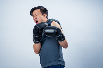 Asian man in sleeveless hoodie wearing boxing gloves strikes forward fighting pose with intense...