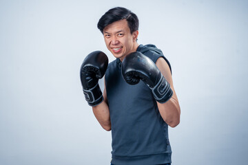 Asian man in sleeveless hoodie wearing boxing gloves strikes forward fighting pose with intense...